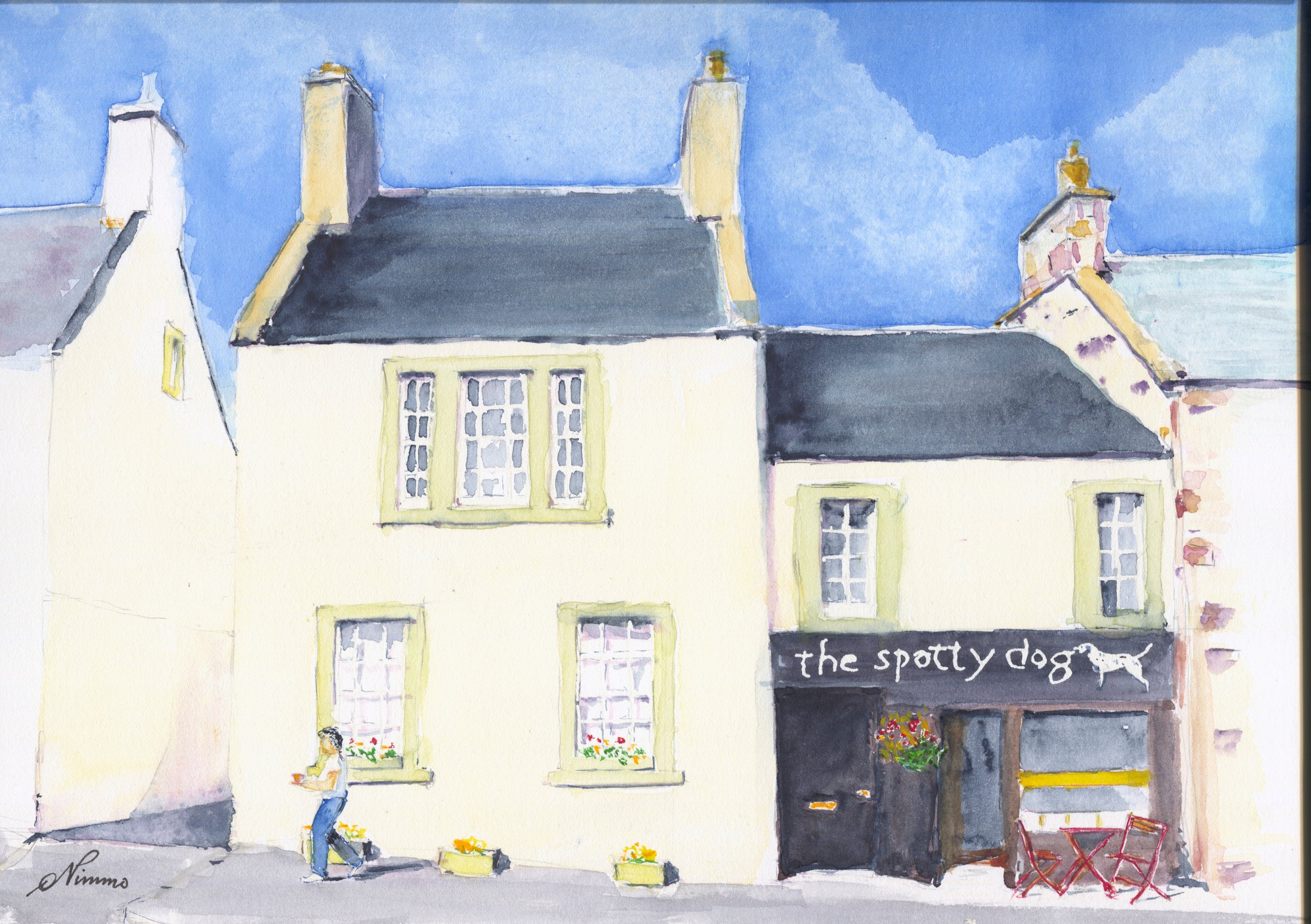 The Spotty Dog shop in Lauder, with a dalmatian on its dark fascia, beside a cream house, with a passer-by, planters and red café chairs.