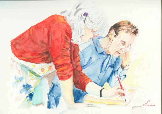 A white-haired woman in a red top leans over a man in a blue shirt and glasses who paints with a red-handled brush at a table covered with a floral cloth.