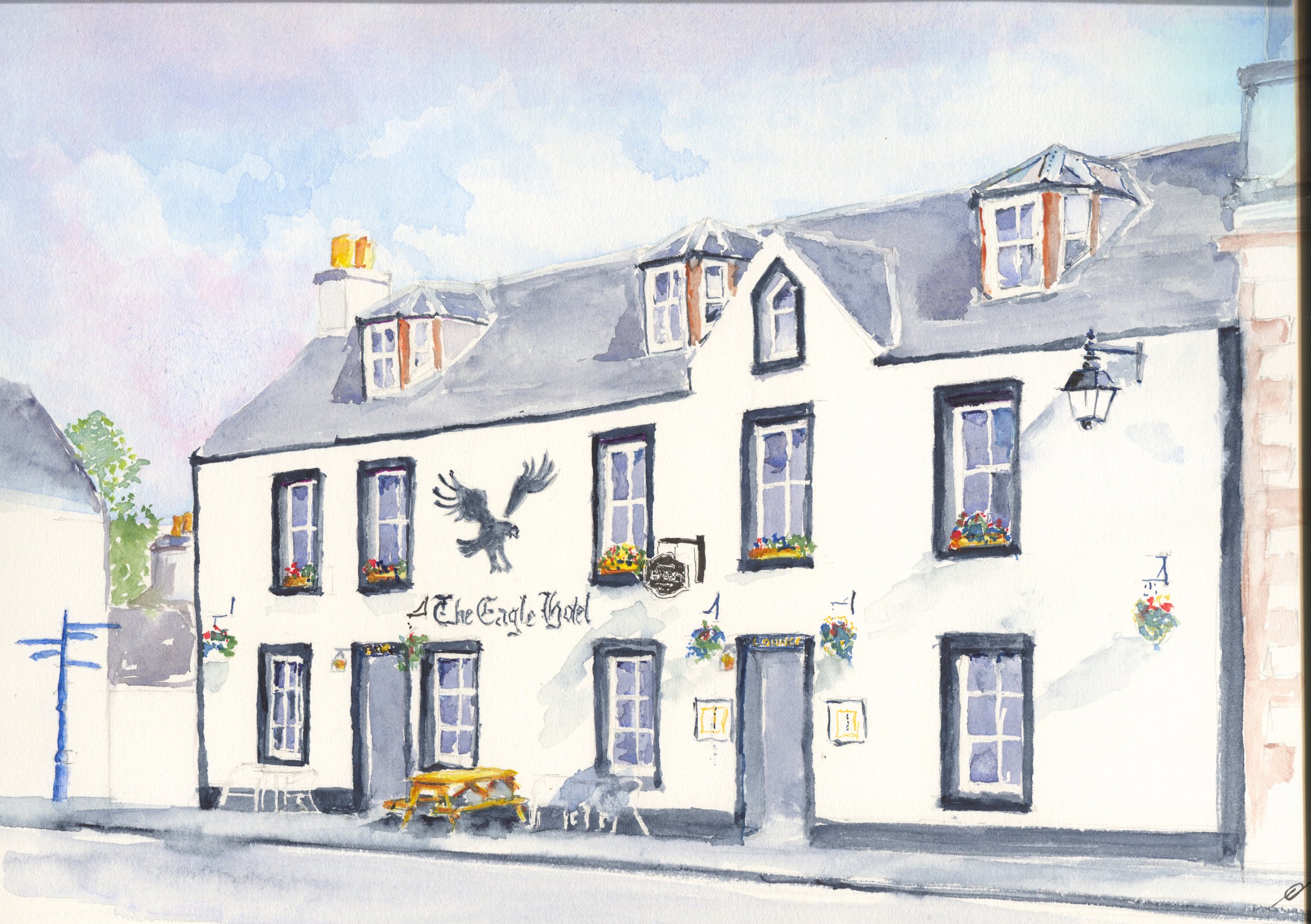The Eagle Hotel in Lauder, a white two-storey building with dormer windows, a painted eagle on the wall, hanging baskets and a picnic bench.