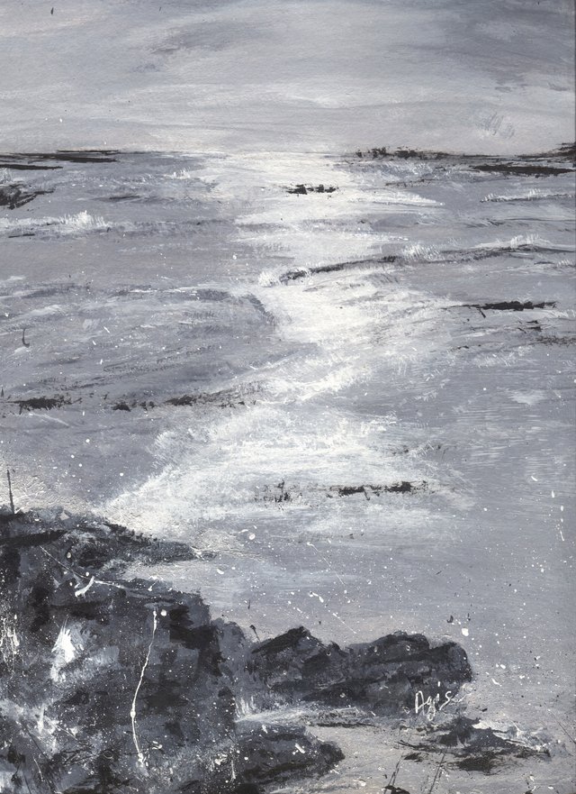 A grey sea under a grey sky, with white light breaking on the water and dark rocks spattered with white in the foreground.